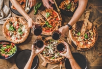 mensen klinken aan tafel met glas wijn en pizza