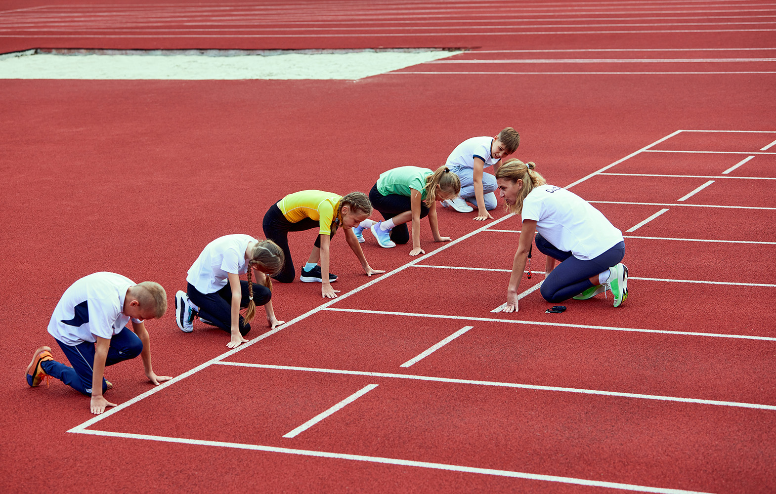 vrouw coacht groep jongeren op atletiekplein